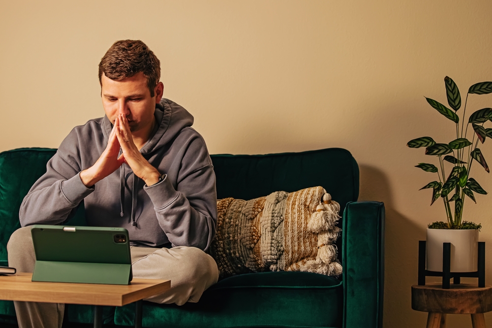 Man looking on the tablet while sitting on his couch. Online therapy, mental health