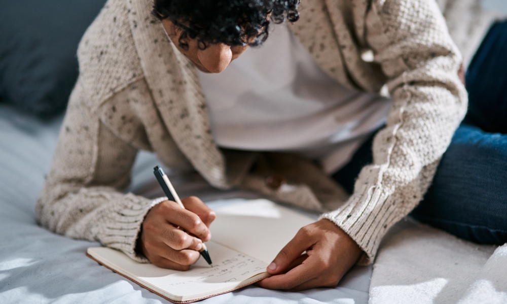 man with journal writing in bed for mental health