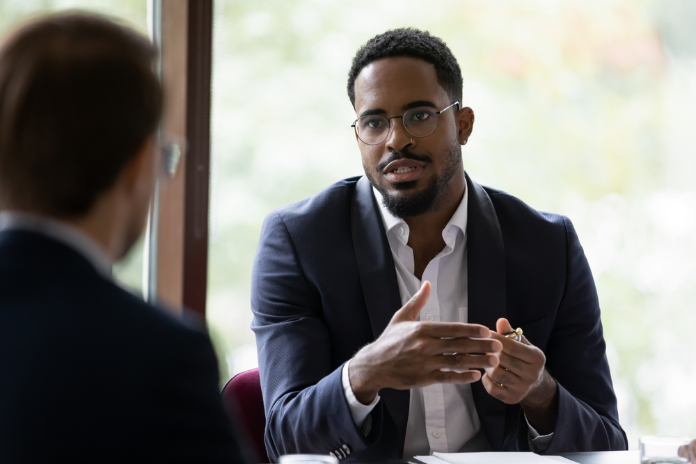 Confident concentrated African American male employee talk with colleague explain thought or idea at office boardroom meeting
