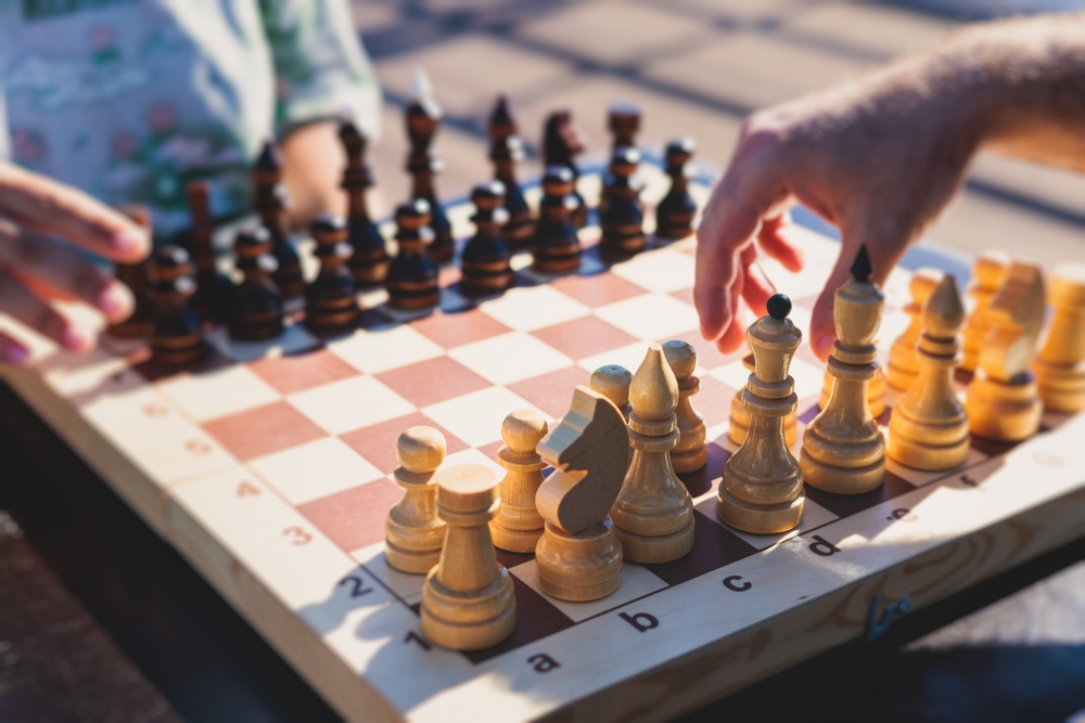 Chess tournament in a summer sunny day, players of all ages play, competition in chess school club with chessboards on a table