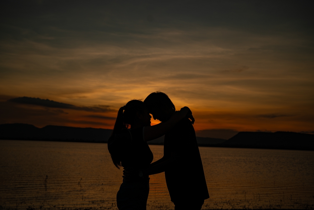 A couple is hugging each other on a beach at sunset